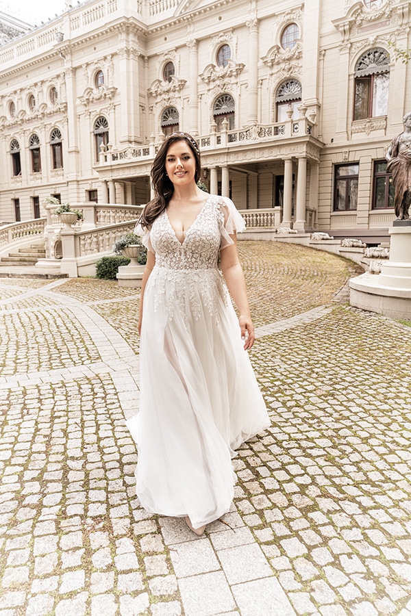 Eine lächelnde Frau mit langen braunen Haaren trägt ein elegantes weißes Kleid vor einem historischen Gebäude