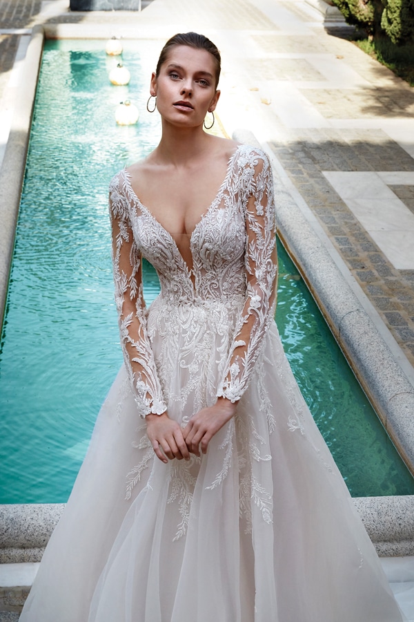 Junge Frau mit ernstem Blick trägt ein elegantes weißes Brautkleid mit Spitzenärmeln