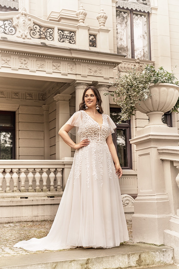 Eine lächelnde Frau im eleganten, weißen Brautkleid steht vor einem historischen Gebäude