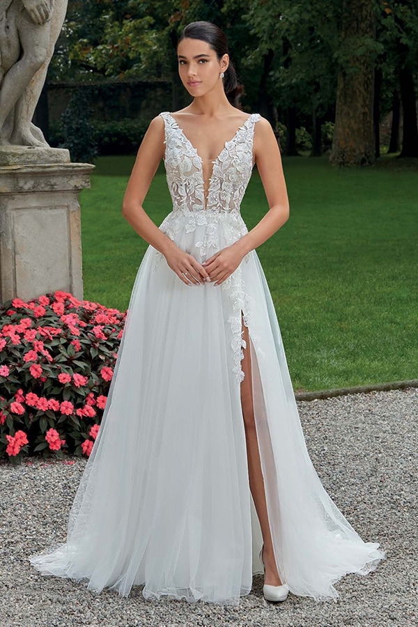 Eine junge Frau steht verträumt in einem weißen Brautkleid mit Spitzendetails und hohem Beinschlitz im Garten