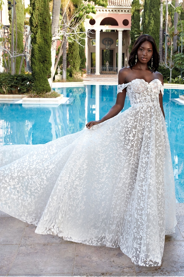 Eine elegante Frau lächelt sanft in einem aufwendigen weißen Spitzenkleid am Pool