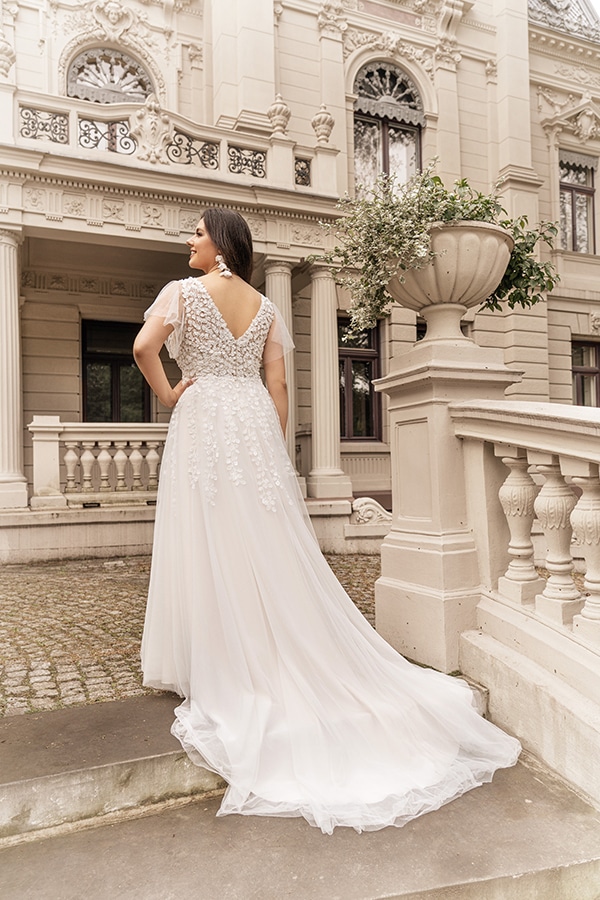 Eine Frau mit dunklen Haaren trägt ein elegantes weißes Kleid vor einem alten Gebäude