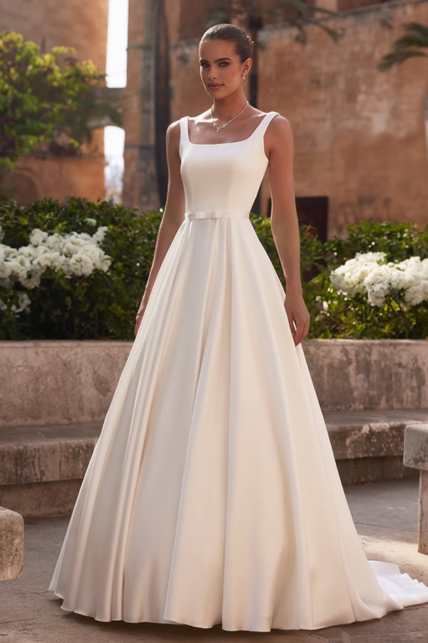 Junge Frau mit elegantem weißen Brautkleid und geschlossenem Lächeln im Garten