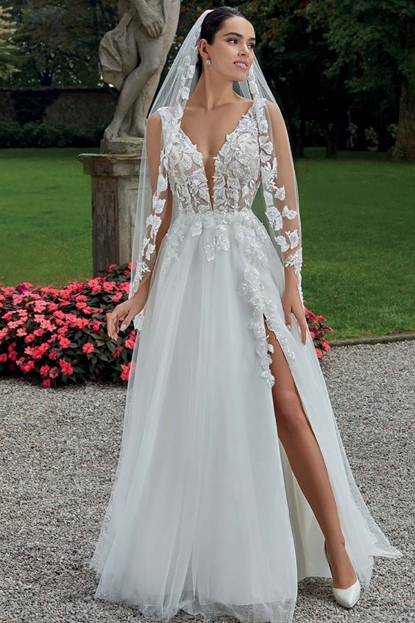 Eine Frau mit elegantem weißen Brautkleid und Schleier lächelt leicht im Garten