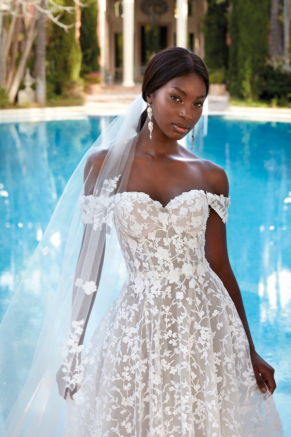 Eine Frau mit ruhigem Gesichtsausdruck trägt ein elegantes weißes Spitzenkleid am Pool