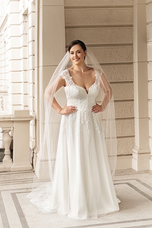 Eine lächelnde Braut im weißen Spitzenkleid mit Schleier posiert auf einem Balkon