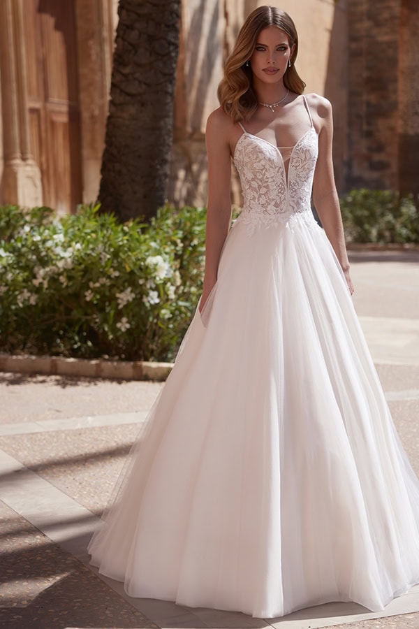 Junge Frau mit langen blonden Haaren lächelt leicht in elegantem weißen Brautkleid