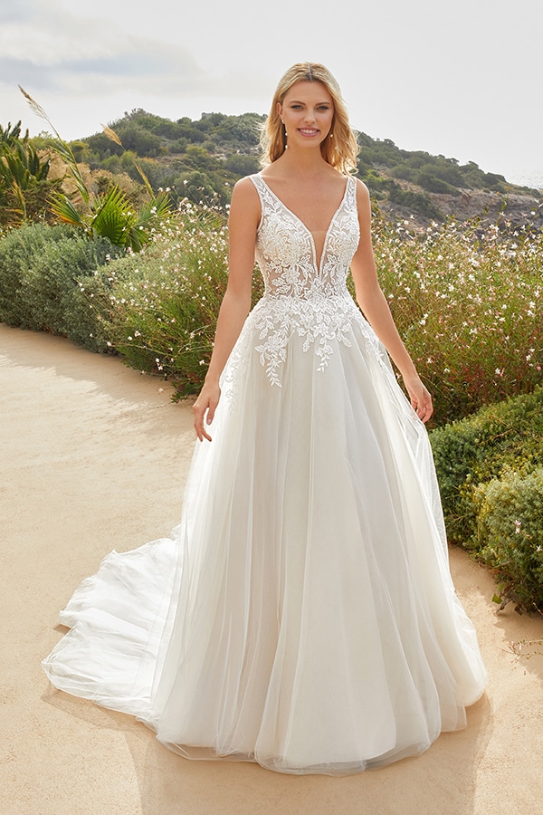 Junge blonde Frau lächelt freundlich in einem weißen Spitzenbrautkleid im Freien