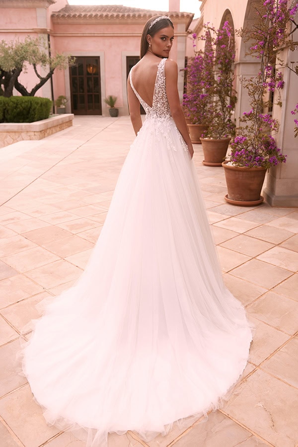 Eine elegante Frau mit ernstem Blick trägt ein weißes Tüllkleid mit Spitzendetails