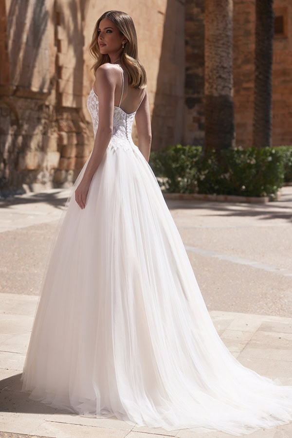 Junge Frau mit langen Haaren in elegantem weißen Brautkleid und Tüllschleppe draußen