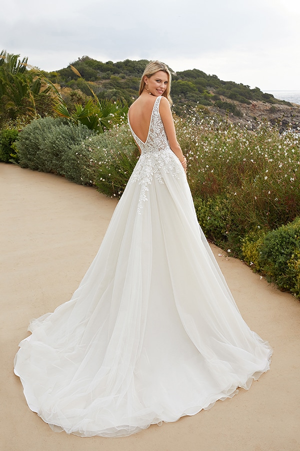 Eine lächelnde blonde Frau trägt ein weißes Brautkleid mit Spitze und Schleppe im Freien