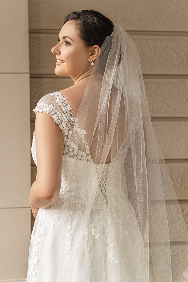 Junge braunhaarige Frau lächelt in eleganten Brautkleid mit Schleier und Spitzenmuster