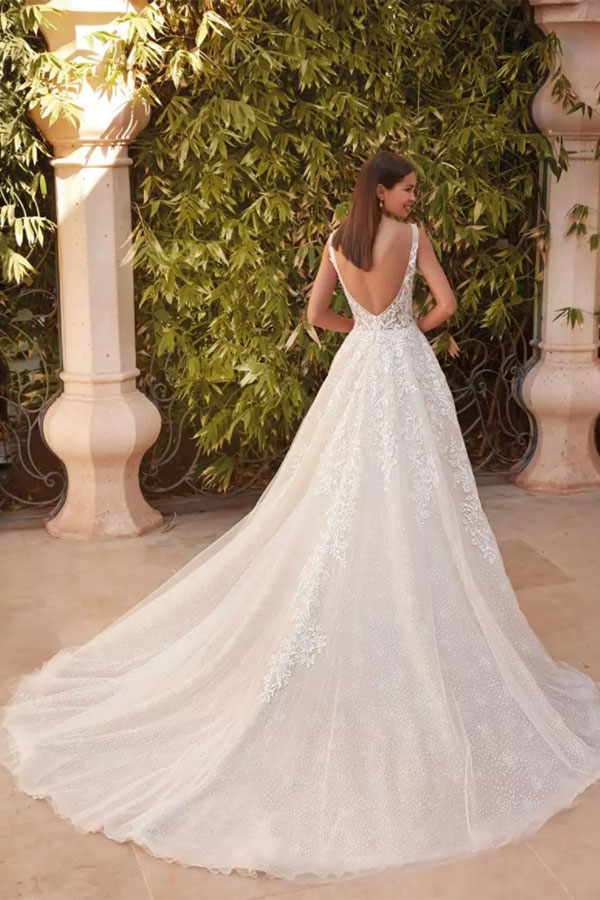 Eine Frau mit langem braunem Haar lacht in einem weißen Spitzenbrautkleid mit Schleppe