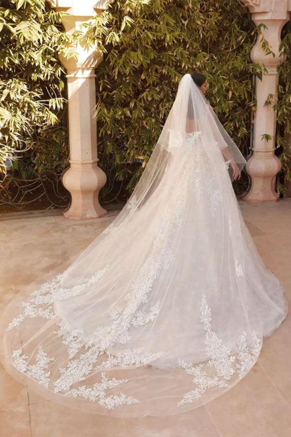 Eine Frau im weißen Brautkleid mit langer Schleppe und Spitzendetails steht draußen