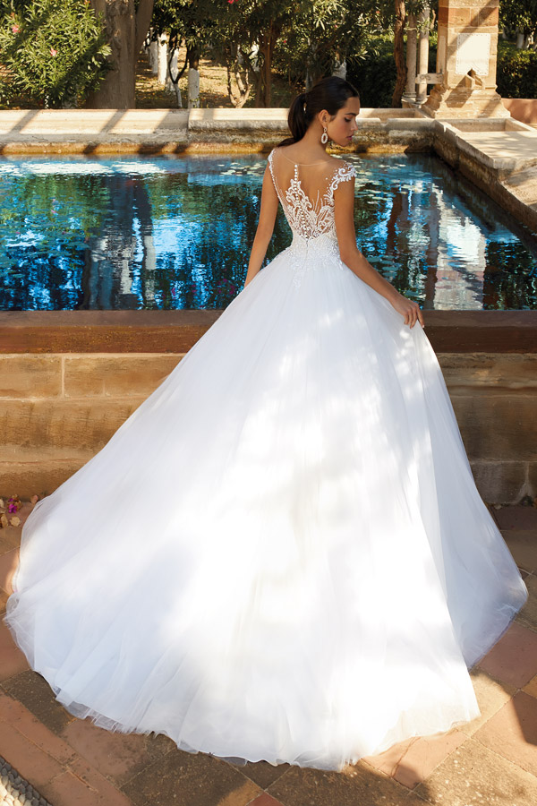 Eine elegant gekleidete Frau mit Hochsteckfrisur trägt ein weißes Spitzenkleid am Pool