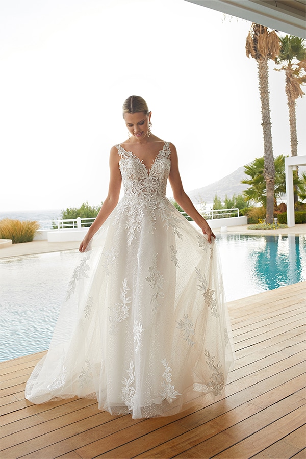 Eine junge Frau lächelt in einem weißen Spitzenkleid am Pool bei sonnigem Wetter