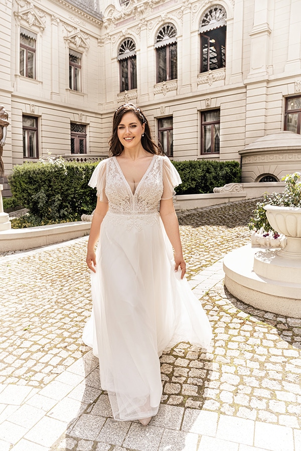 Eine lächelnde Frau im cremefarbenen Brautkleid steht vor einem historischen Gebäude