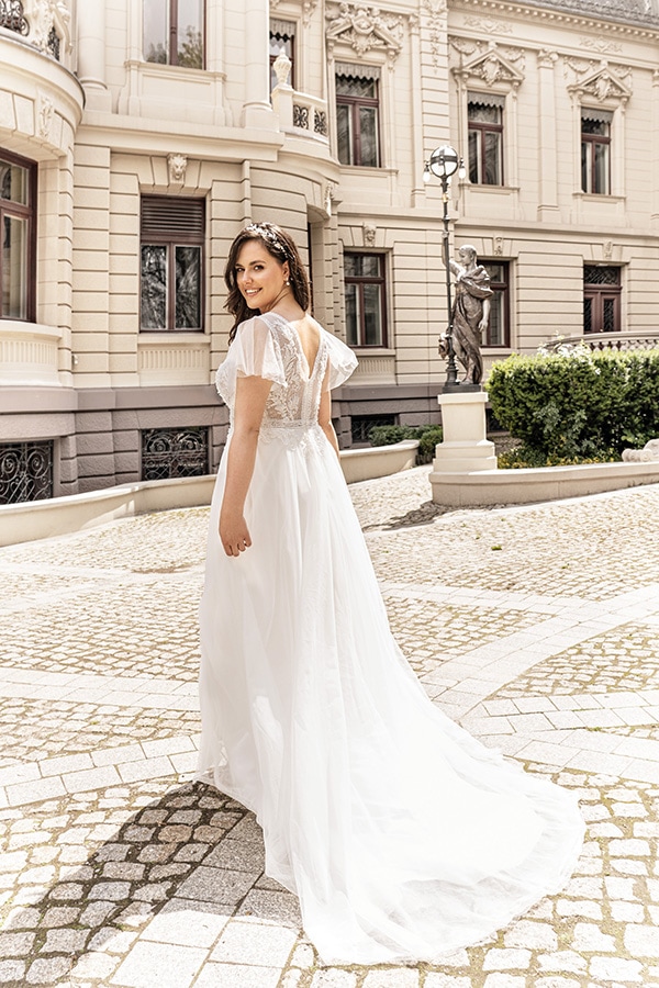 Eine lächelnde Frau im weißen Brautkleid steht vor einem historischen Gebäude