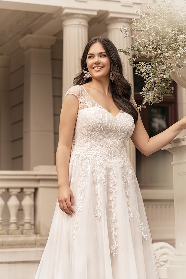 Frau im weißen Spitzenkleid lächelt freundlich und steht vor klassischer Architektur