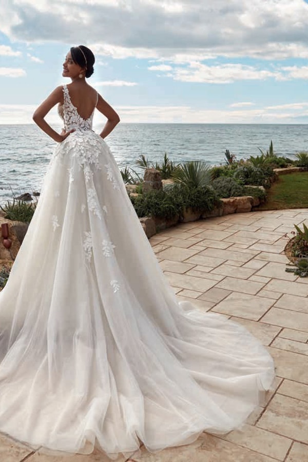 Eine Frau in einem eleganten weißen Brautkleid blickt lächelnd aufs Meer