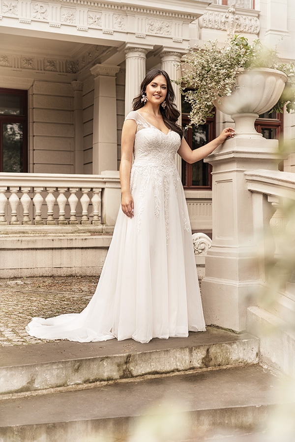 Eine lächelnde Frau im weißen Brautkleid steht elegant vor einem historischen Gebäude