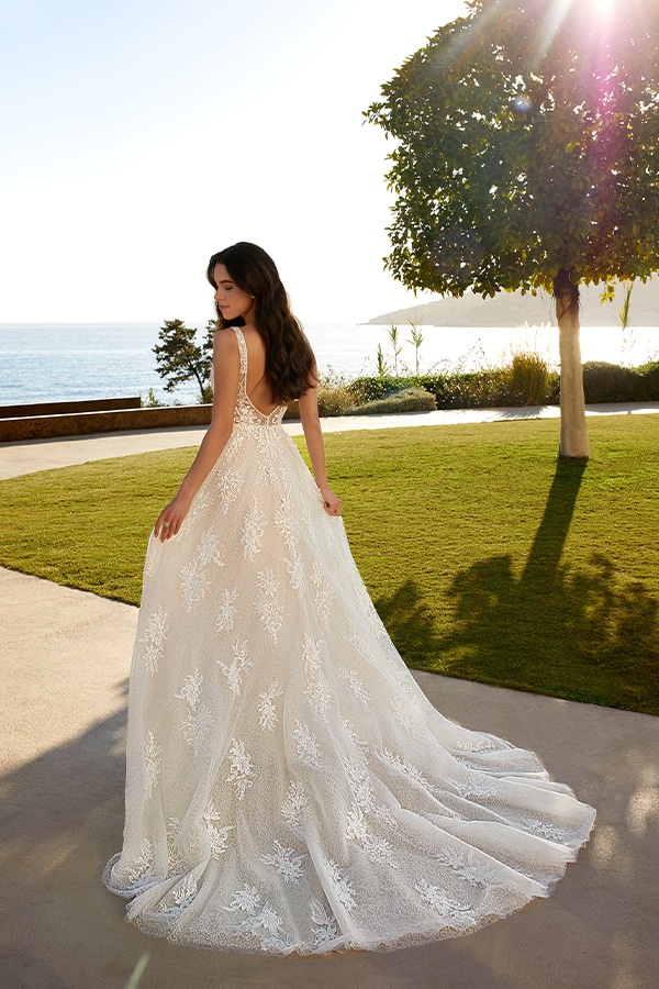 Junge Frau in einem cremefarbenen Spitzenkleid blickt lächelnd aufs Meer