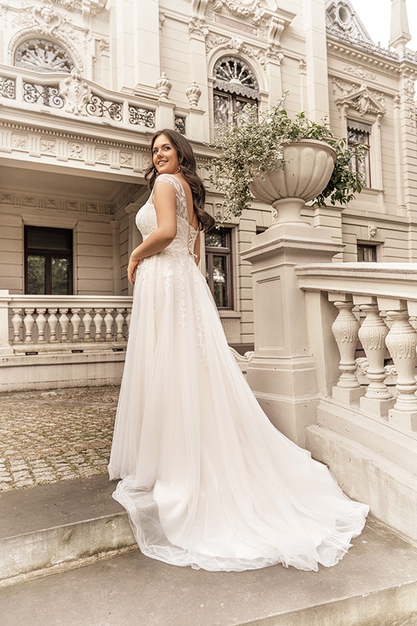 Eine lächelnde Frau im weißen Brautkleid steht vor einem historischen Gebäude