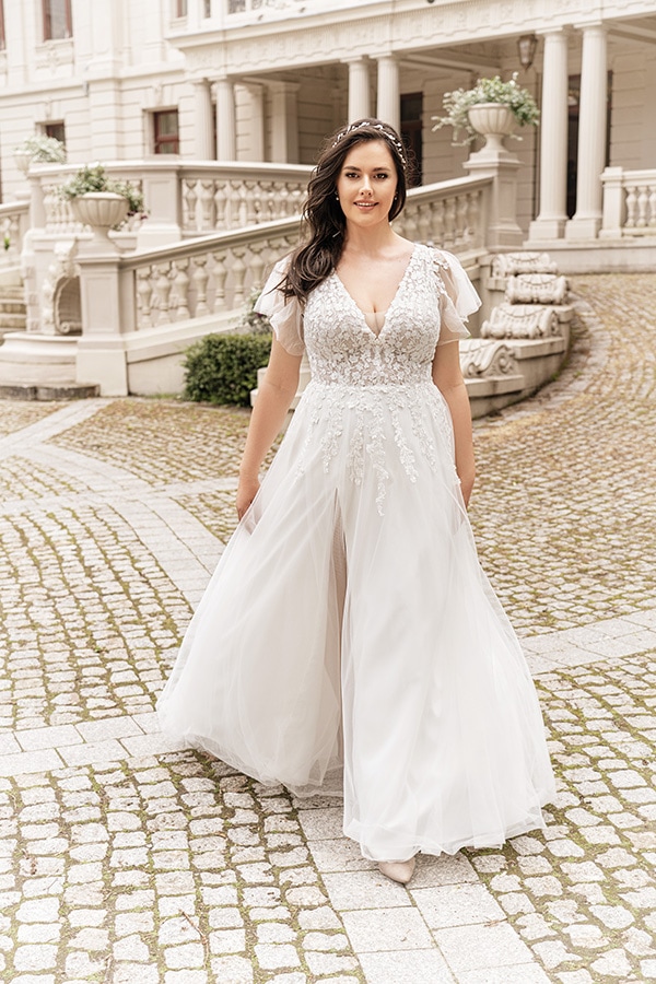 Eine lächelnde Frau mit dunklem Haar trägt ein elegantes weißes Brautkleid