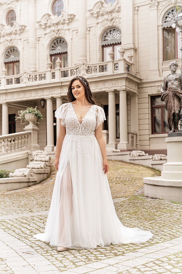 Junge Frau mit langen dunklen Haaren lächelt in weißem Spitzenkleid vor historischem Gebäude