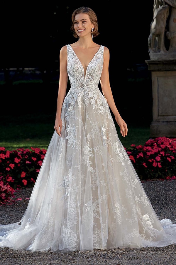 Eine lächelnde Frau steht im eleganten weißen Brautkleid mit floraler Spitze
