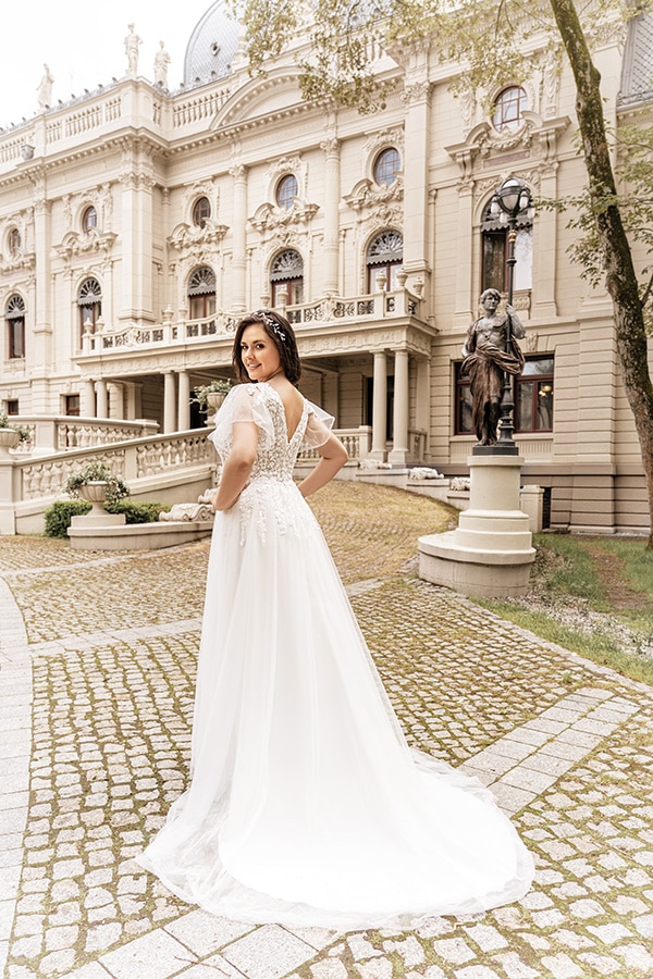 Eine Frau im weißen Brautkleid schaut lächelnd über die Schulter vor einem Schloss