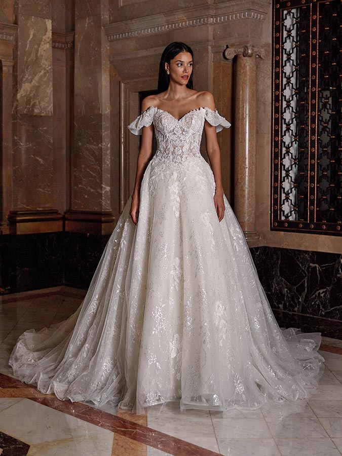 Eine junge Frau in weißem Brautkleid mit Spitzen und Herzausschnitt schaut ernst