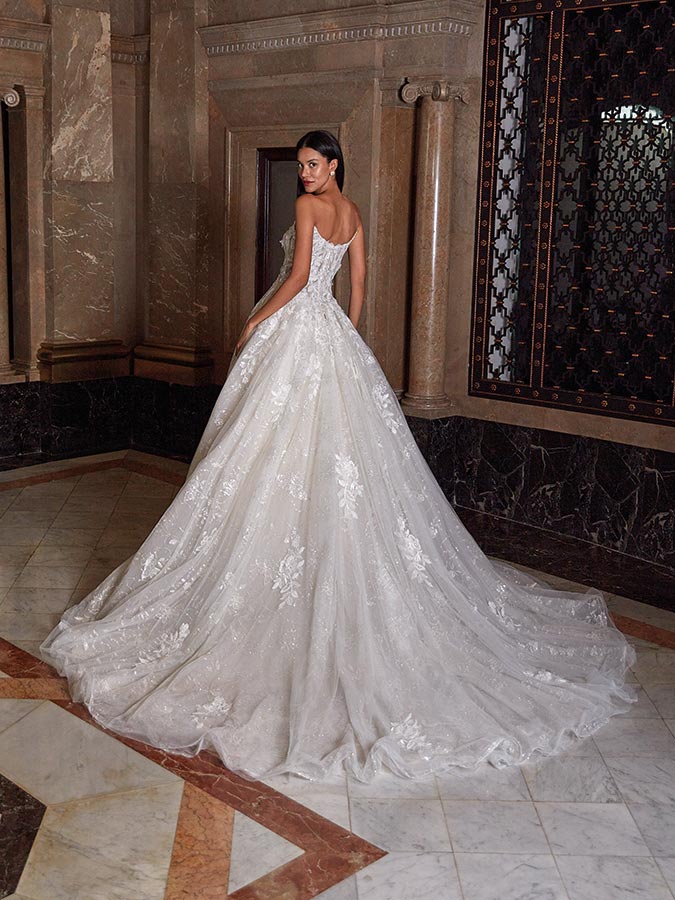 Eine Frau im weißen Brautkleid steht elegant vor Marmorwänden und blickt zurück