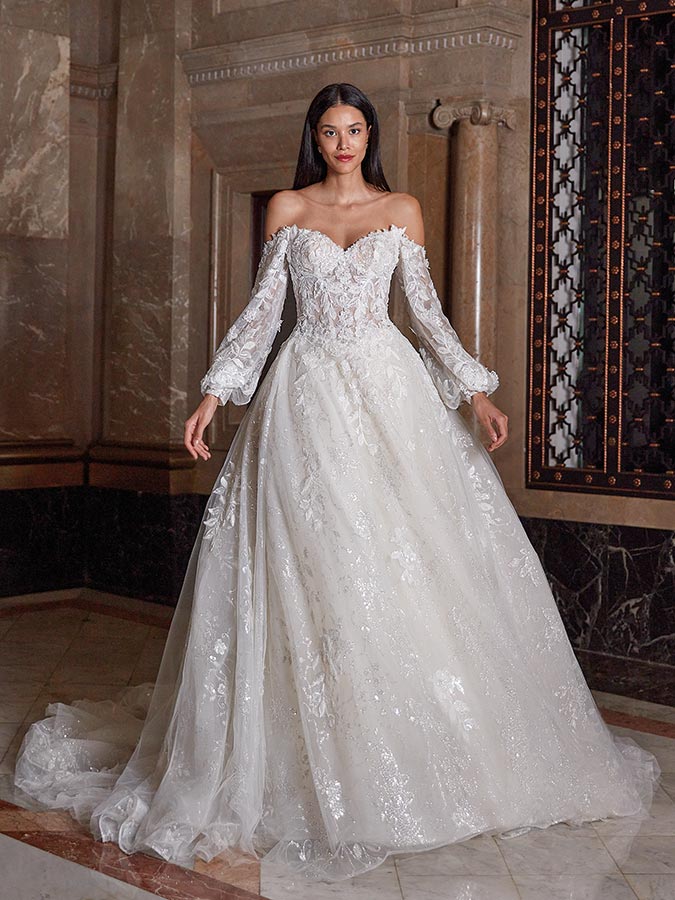 Eine junge Frau mit ruhigem Gesicht trägt ein weißes Spitzenkleid mit langen Ärmeln