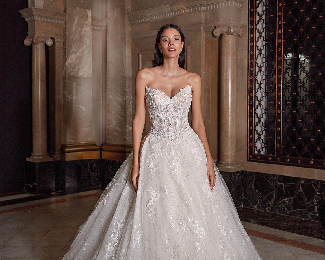 Eine Frau mit langen dunklen Haaren trägt ein elegantes weißes Brautkleid und blickt ernst