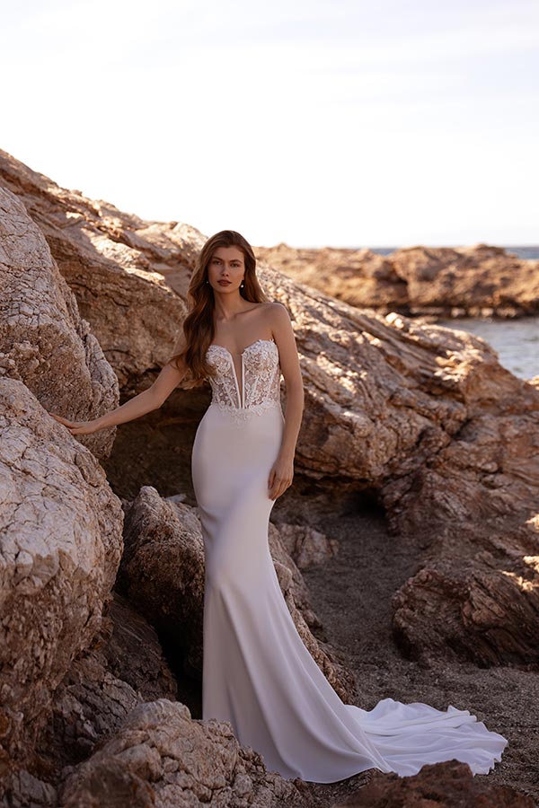 Eine Frau mit langen braunen Haaren im eleganten weißen Brautkleid am Felsstrand