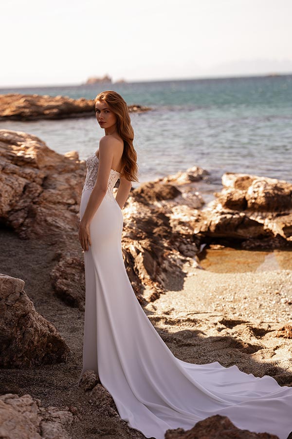 Eine Frau mit langen roten Haaren in einem eleganten weißen Brautkleid am Strand
