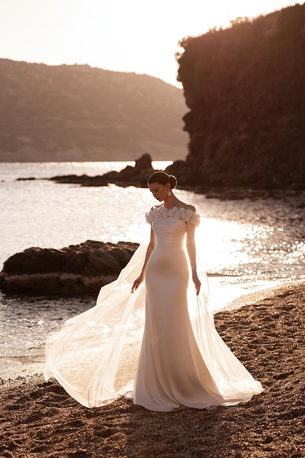 Eine Frau im eleganten weißen Kleid steht verträumt am sonnigen Strand