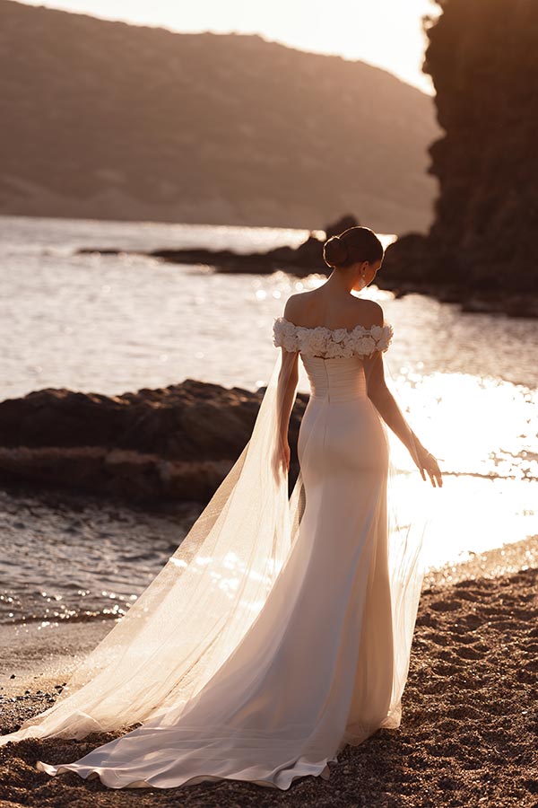 Eine Frau im eleganten weißen Brautkleid steht am sonnigen Seeufer und blickt zurück