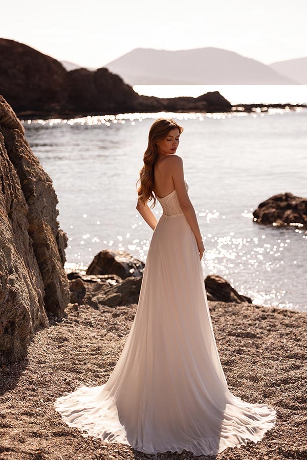 Eine Frau im eleganten cremefarbenen Kleid steht am sonnigen Strand und blickt zurück