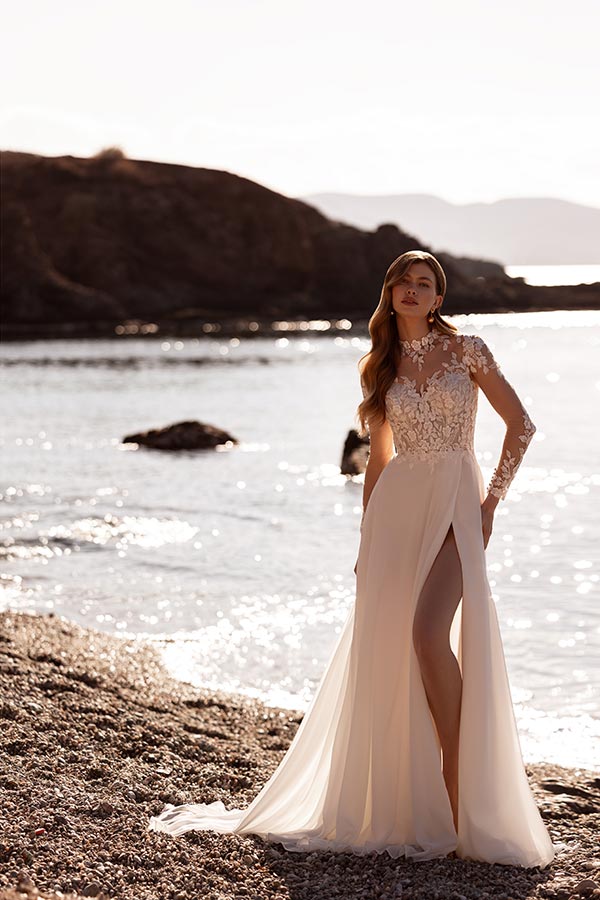 Eine junge Frau mit langem Haar in einem eleganten cremefarbenen Brautkleid am Strand