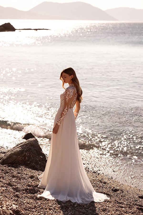 Eine junge Frau im eleganten weißen Spitzenkleid steht nachdenklich am sonnigen Meer