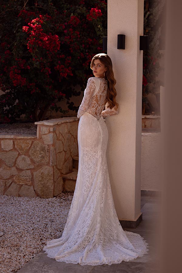 Eine Frau mit langen braunen Haaren trägt ein elegantes weißes Spitzenkleid und blickt verträumt zurück