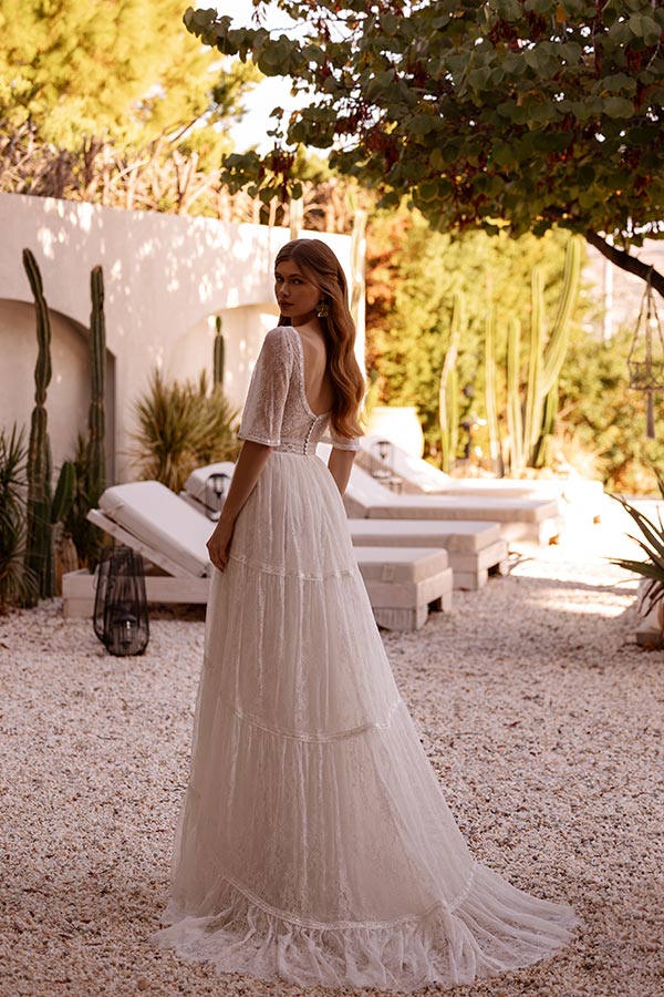 Eine junge Frau im eleganten weißen Spitzenkleid blickt lächelnd über die Schulter