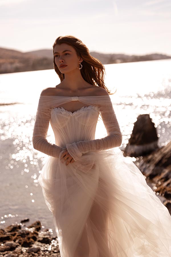 Junge Frau mit entspannter Miene im weißen Brautkleid vor sonnigem Wasser