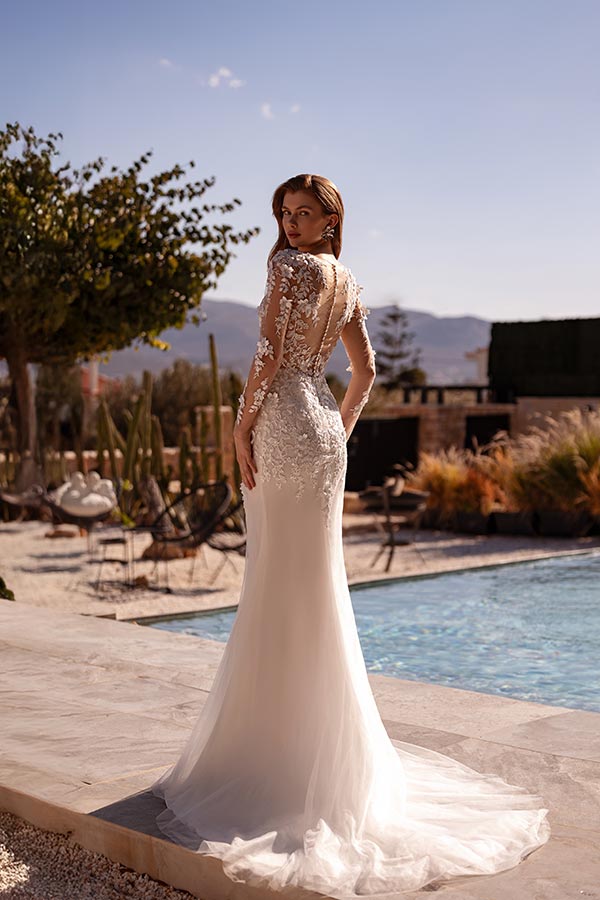 Eine Frau mit langen braunen Haaren steht im eleganten Spitzenkleid am Pool und blickt zurück