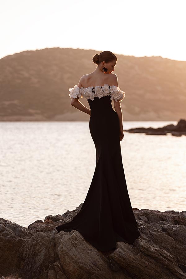 Eine elegant gekleidete Frau im schwarzen Kleid mit weißen Blumen am Ufer bei Sonnenuntergang