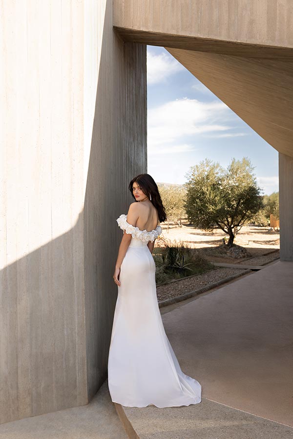 Eine Frau mit dunklem Haar und lächelndem Gesicht trägt ein elegantes weißes Kleid