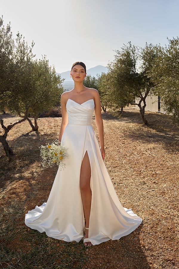 Eine Frau mit ernstem Blick trägt ein elegantes weißes Brautkleid und hält Blumen