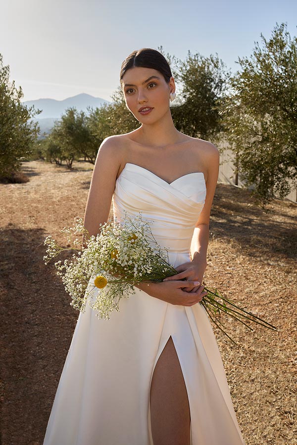 Junge Frau im cremeweißen Brautkleid mit Blumenstrauß blickt ruhig in die Kamera